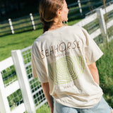 Beige cotton Seahorse classic tee with black wordmark logo on front, unisex fit worn outdoors