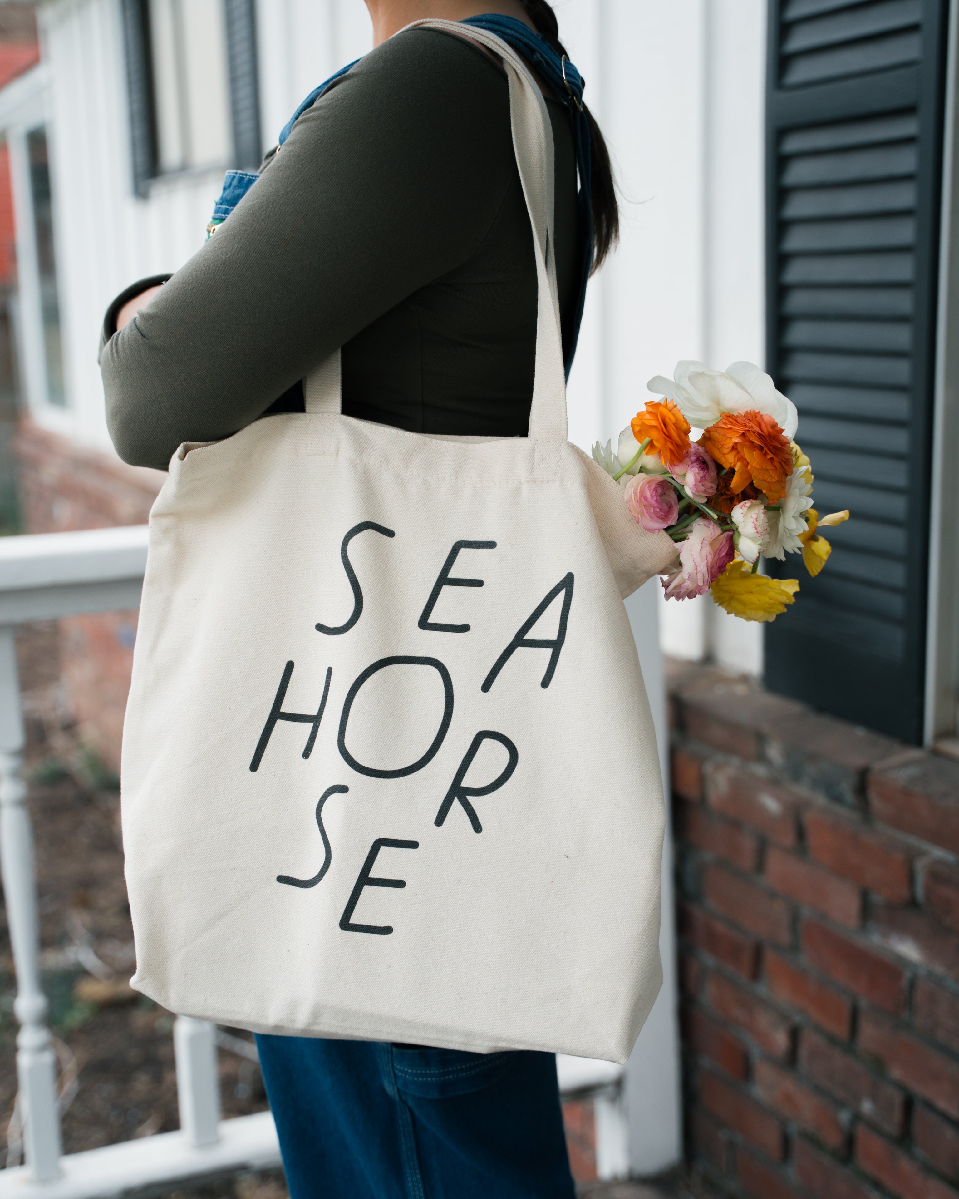 Cotton canvas Seahorse tote bag with black wordmark, worn over shoulder outdoors with flowers inside